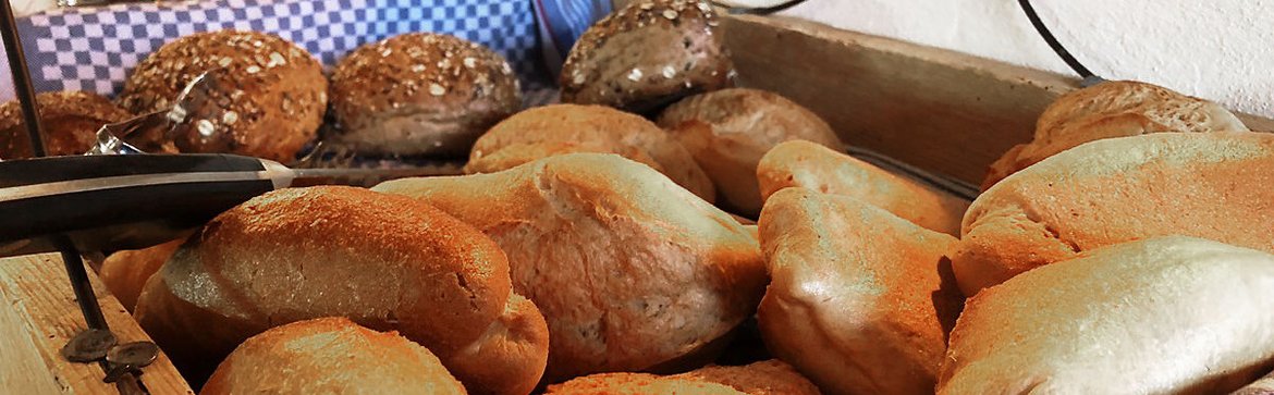 Verschiedene Brötchensorten in einer Holzkiste, ein Brotmesser mit schwarzem Griff liegt ebenfalls darin