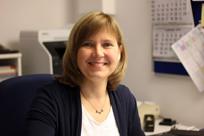 Sylke Bork hat schulterlanges blondes Haar. Sie hat ein helles Oberteil mit einem dunklen Blazer darüber. Sie sitzt vor dem Schreibtisch. An der Wand hängt ein aufgeklappter Kalender und sie lächelt freundlich in die Kamera. - Copyright: Thomas Moll 