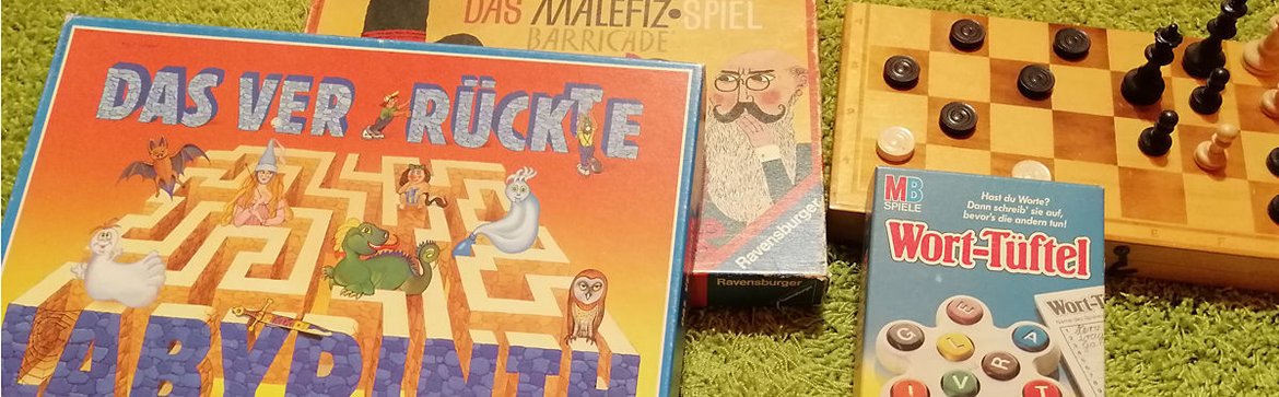 Verschiedene Spiele liegen auf einem grünen Teppich (Das verrückte Labyrinth, Malefiz, ein Schach- bzw. Damebrett, Wort-Tüftel